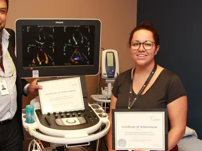 Staff holding a certificate beside an echo machine