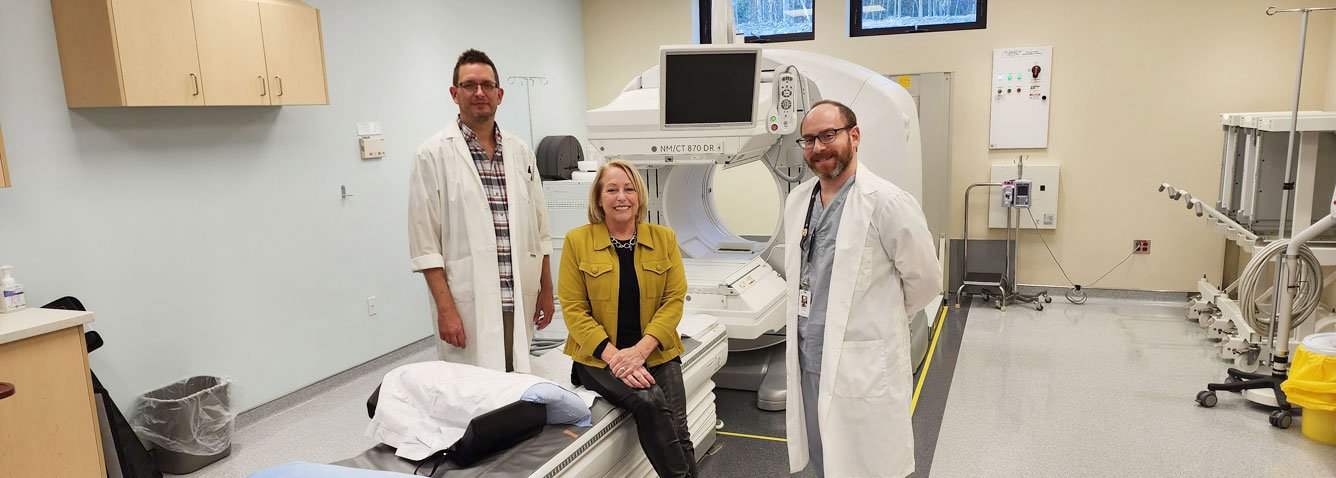 Three people standing with the SPECT-CT Nuclear Medicine machine